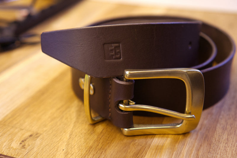 Brown leather belt with brass buckle on a wooden surface