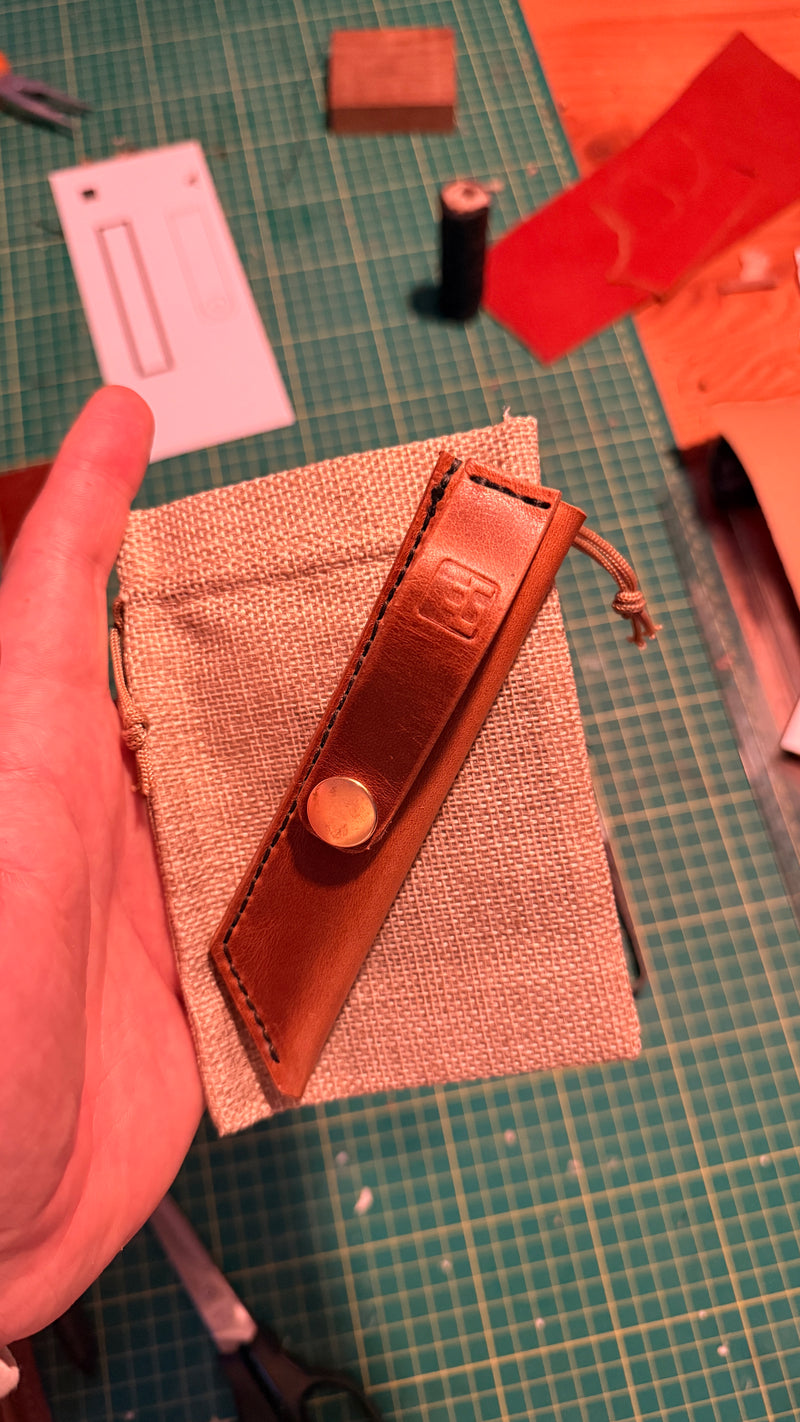 Handmade leather sheath on a textured surface with tools in the background