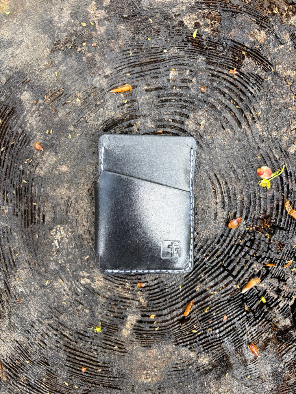 Black leather wallet on a textured surface with leaves