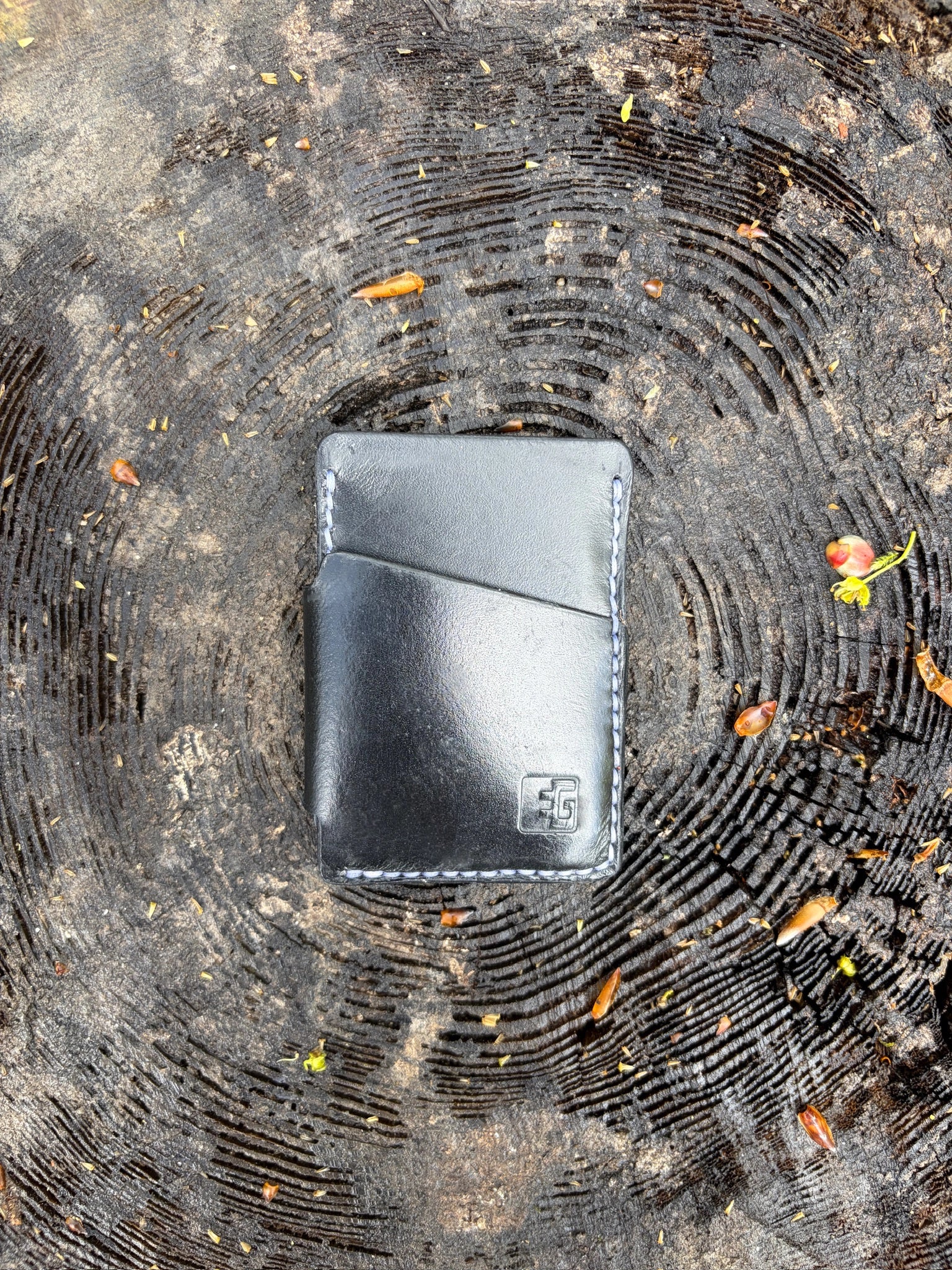 Black leather wallet on a textured surface with leaves
