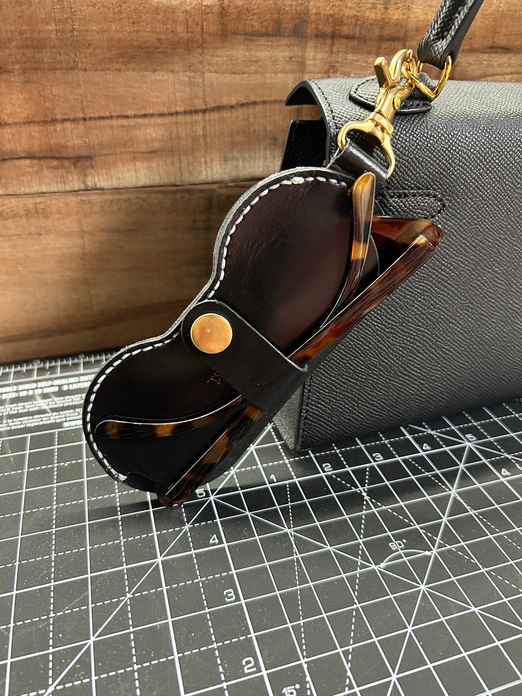 Black leather sunglasses case with tortoiseshell sunglasses on a gray textured surface.
