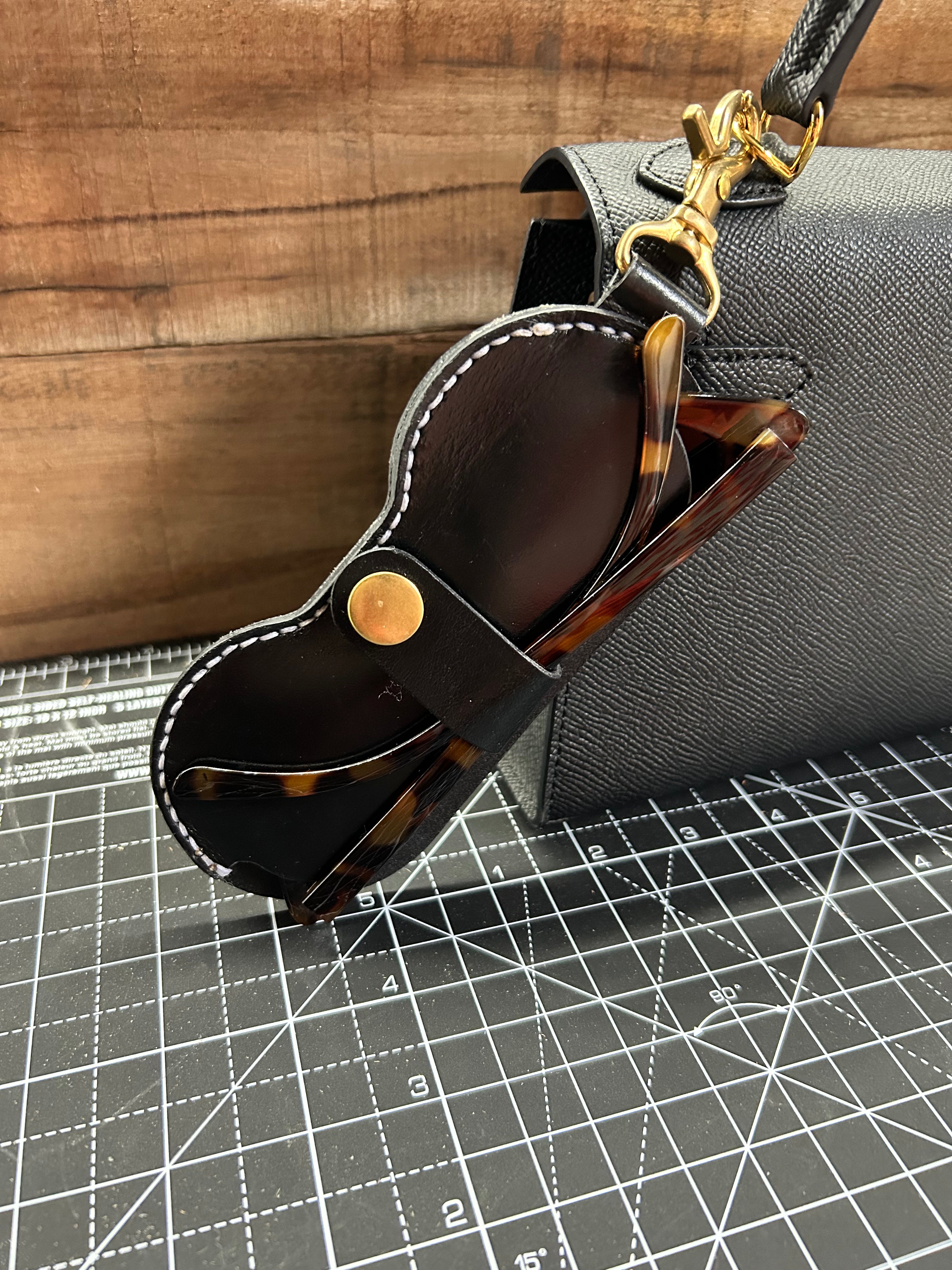 Black leather sunglasses case with tortoiseshell sunglasses on a gray textured surface.