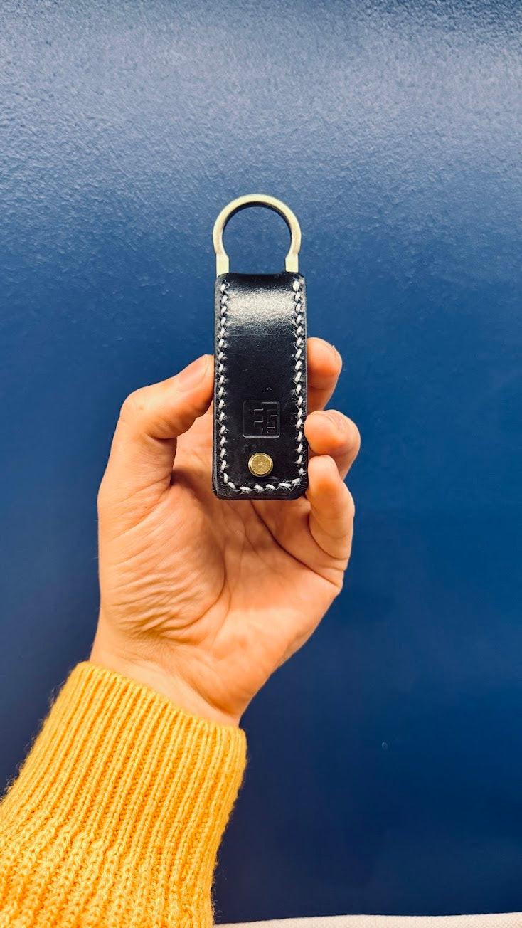 Hand holding a black leather key fob against a blue background