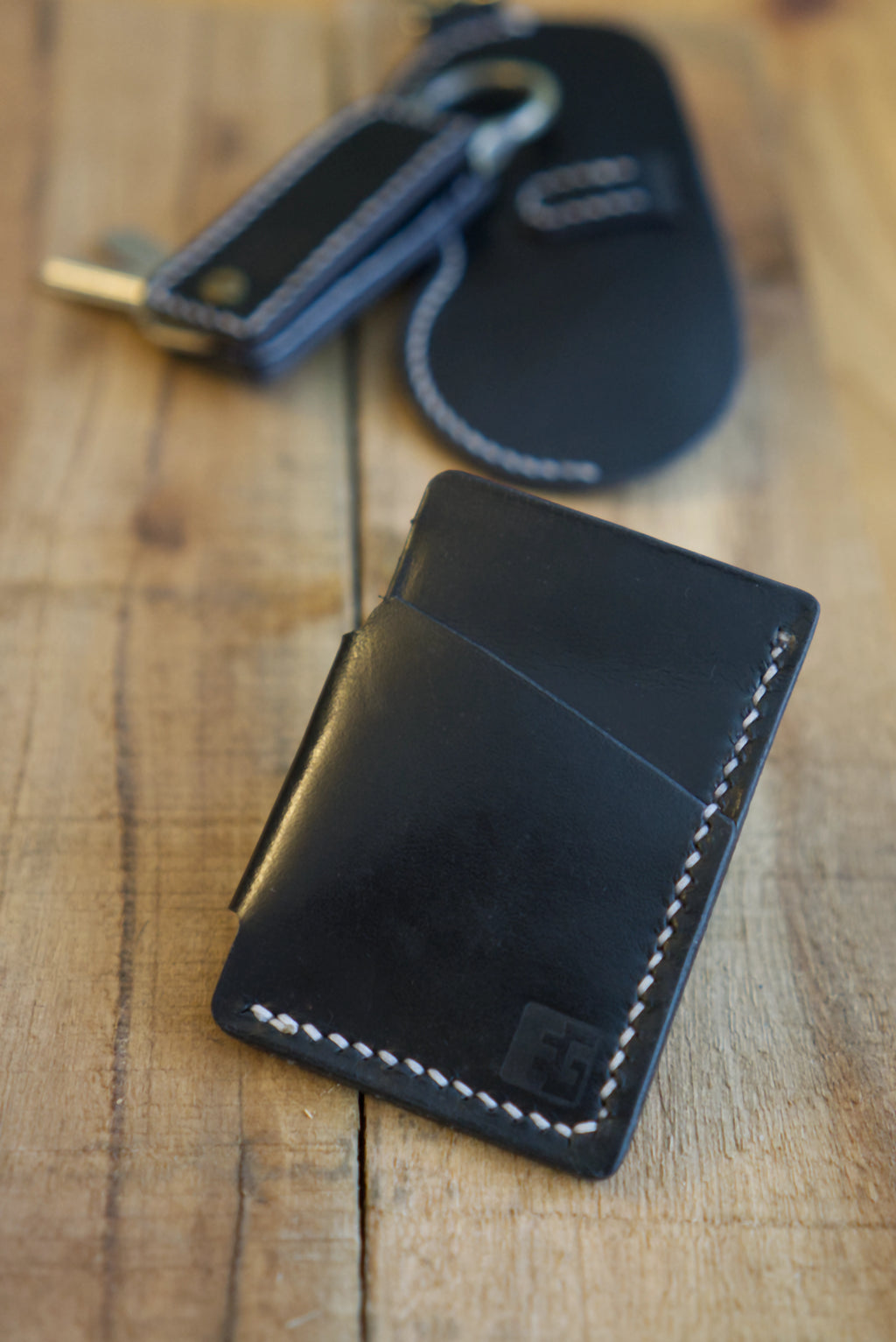 Black leather wallet with key holder & glasses cases in the background on a wooden surface