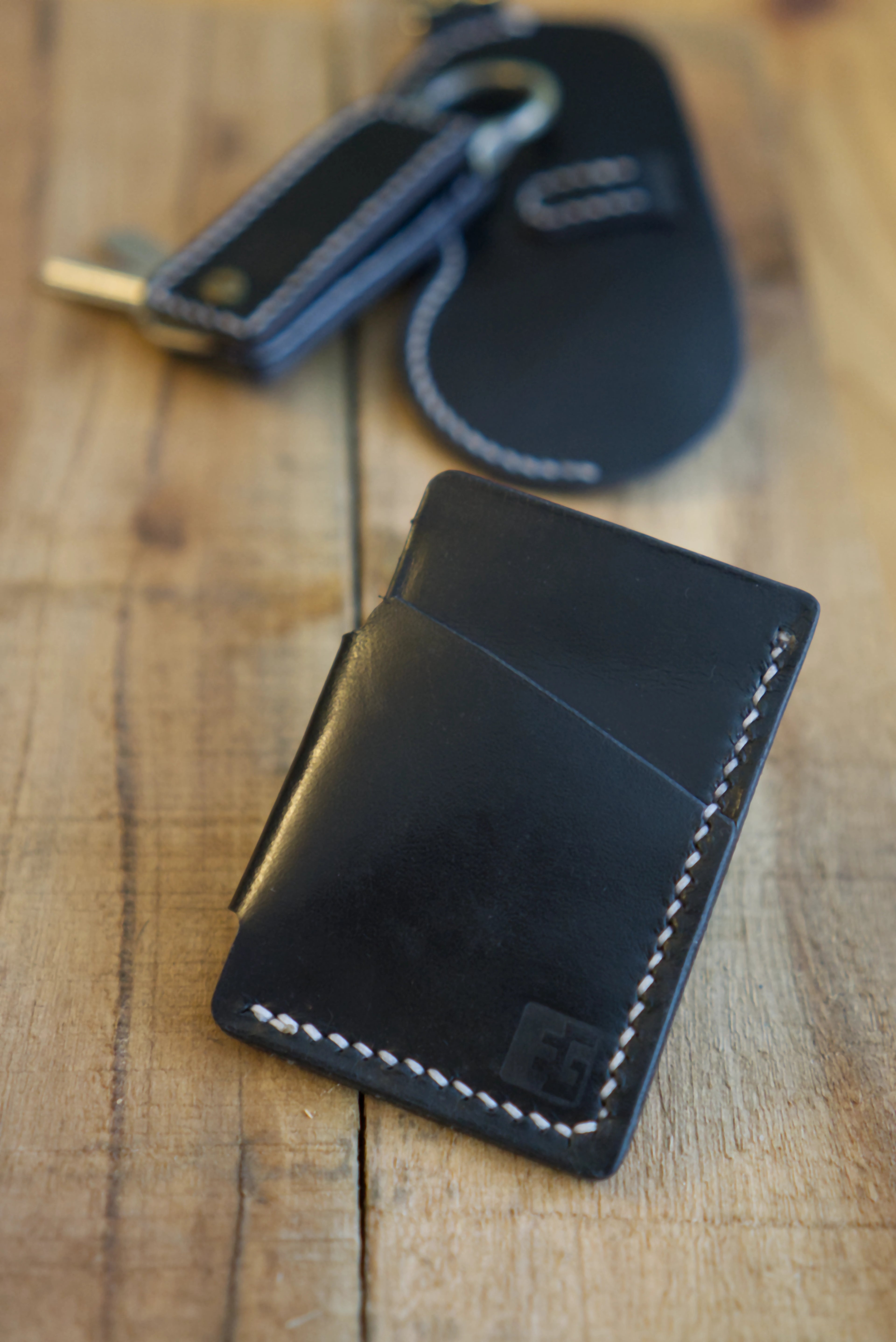 Black leather wallet with key holder & glasses cases in the background on a wooden surface