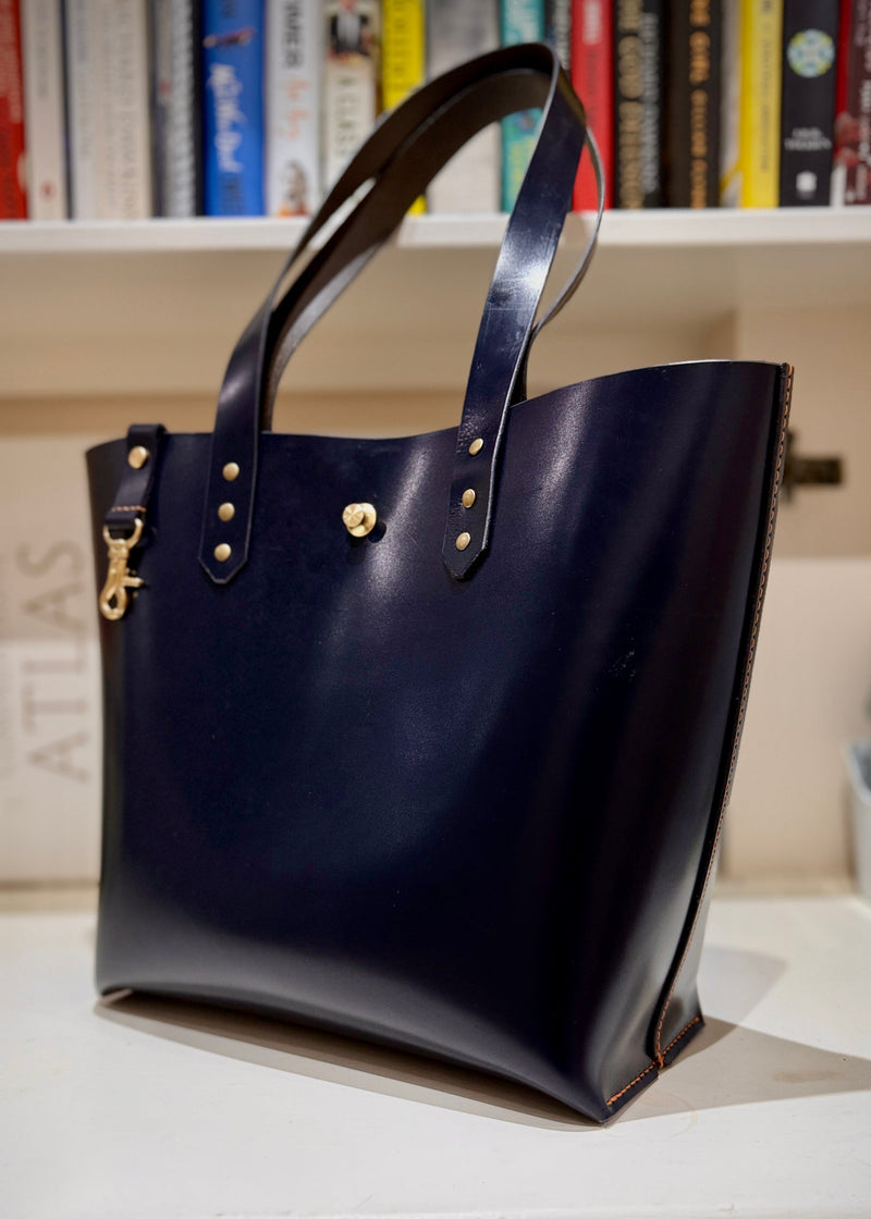 Navy blue handbag with gold accents on a white surface with books in the background