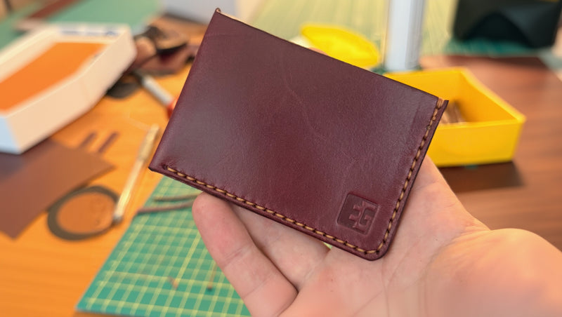 red leather wallet held in a hand with a blurred craft workspace in the background