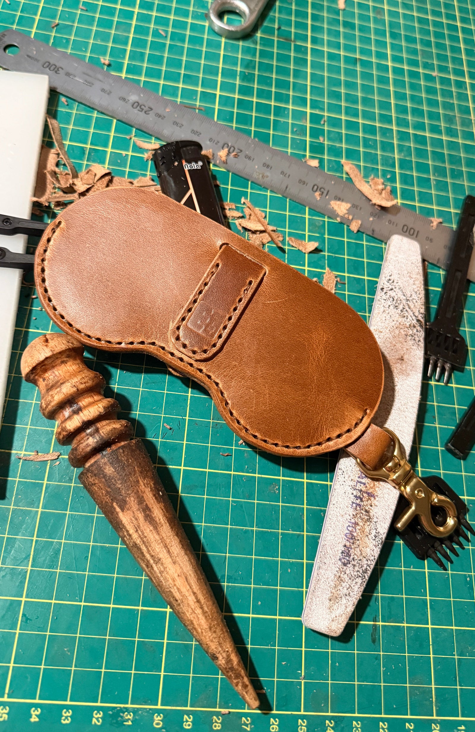 Brown leather Glasses Case with wooden slicker on a green cutting mat with tools.
