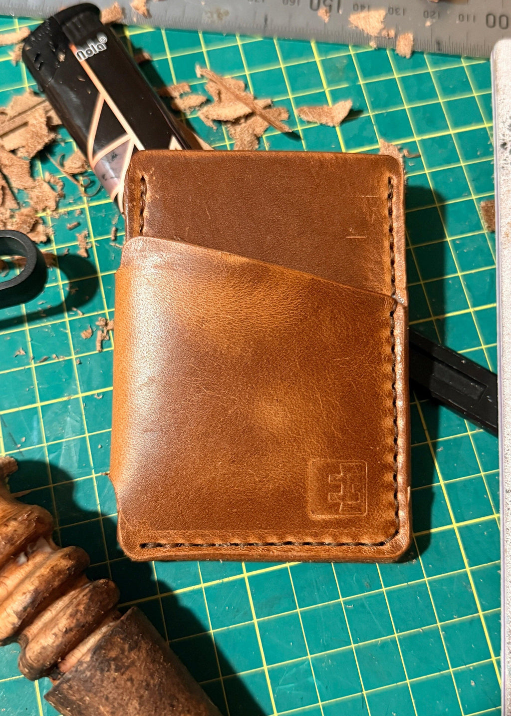 Brown leather wallet on a green cutting mat with tools and a ruler.