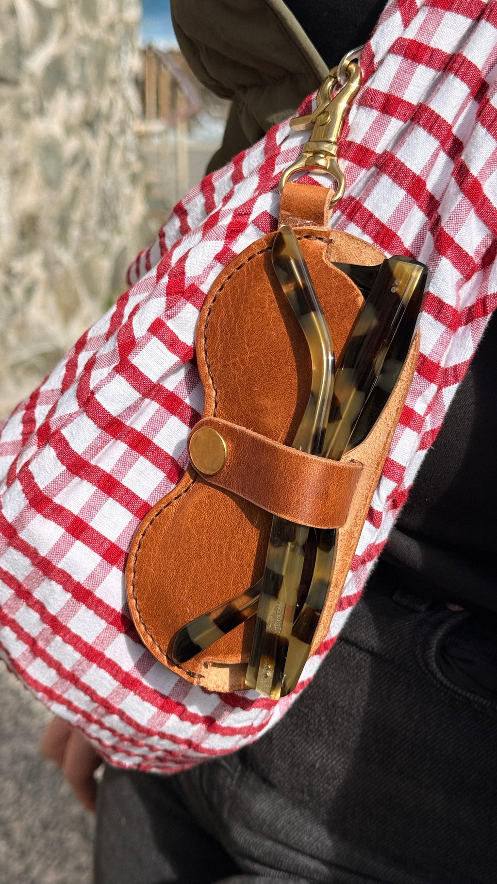Close-up of sunglasses with a brown leather case and red checkered fabric