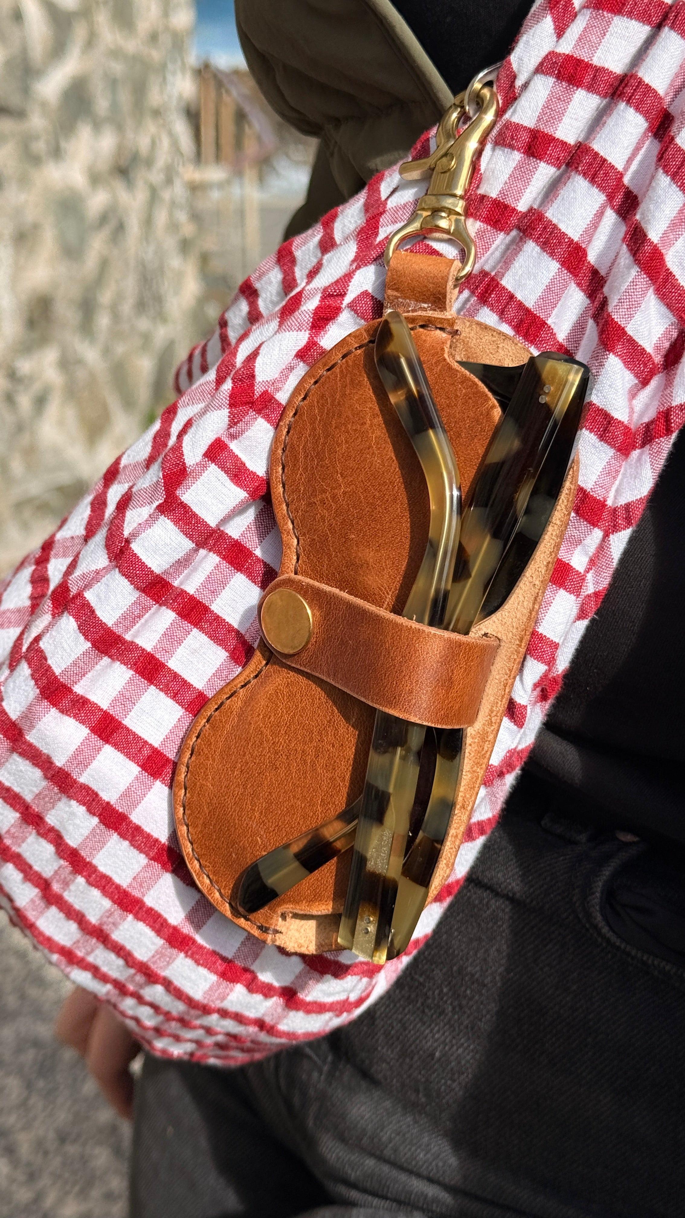 Close-up of sunglasses with a brown leather case and red checkered fabric
