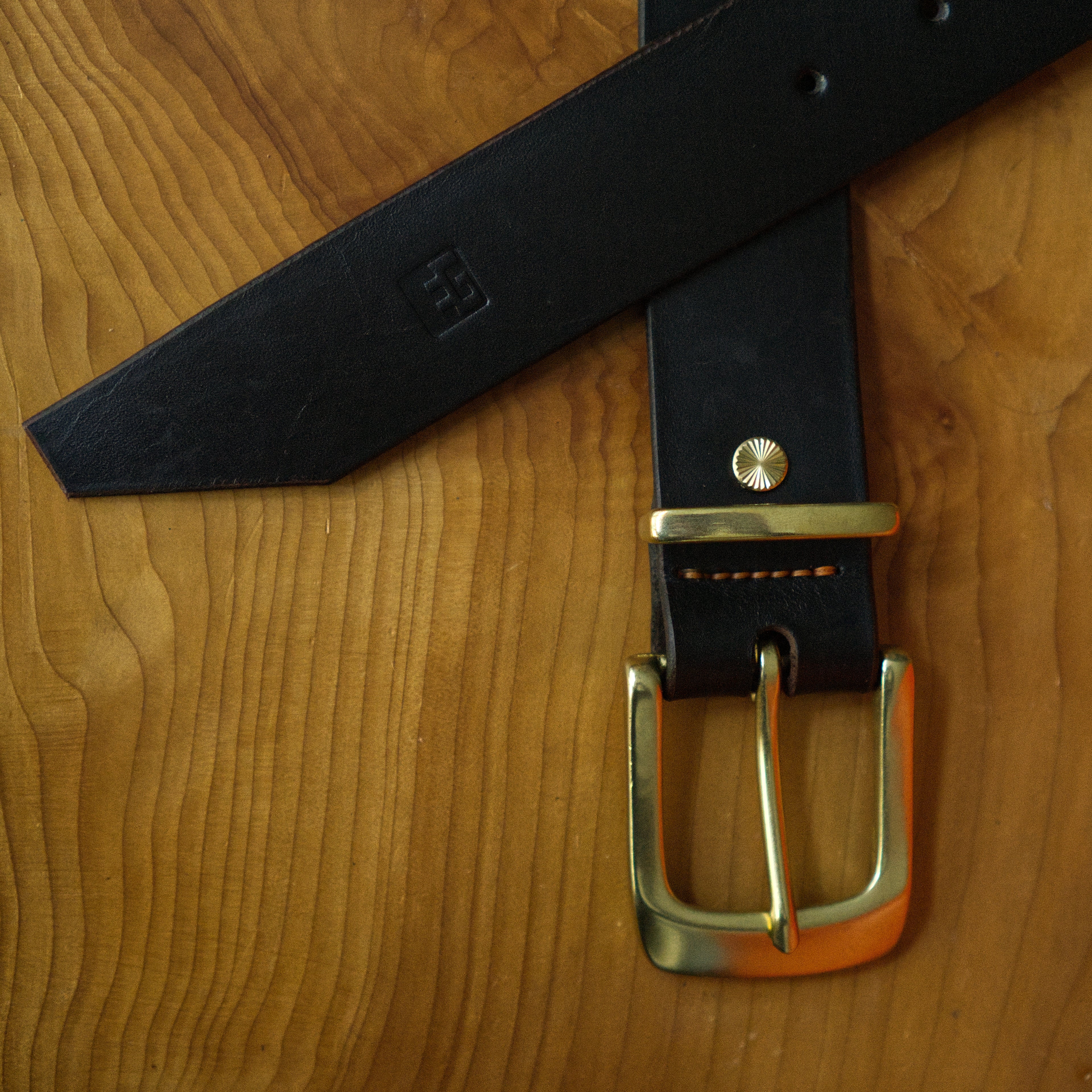 Brown leather belt with brass buckle on a wooden surface