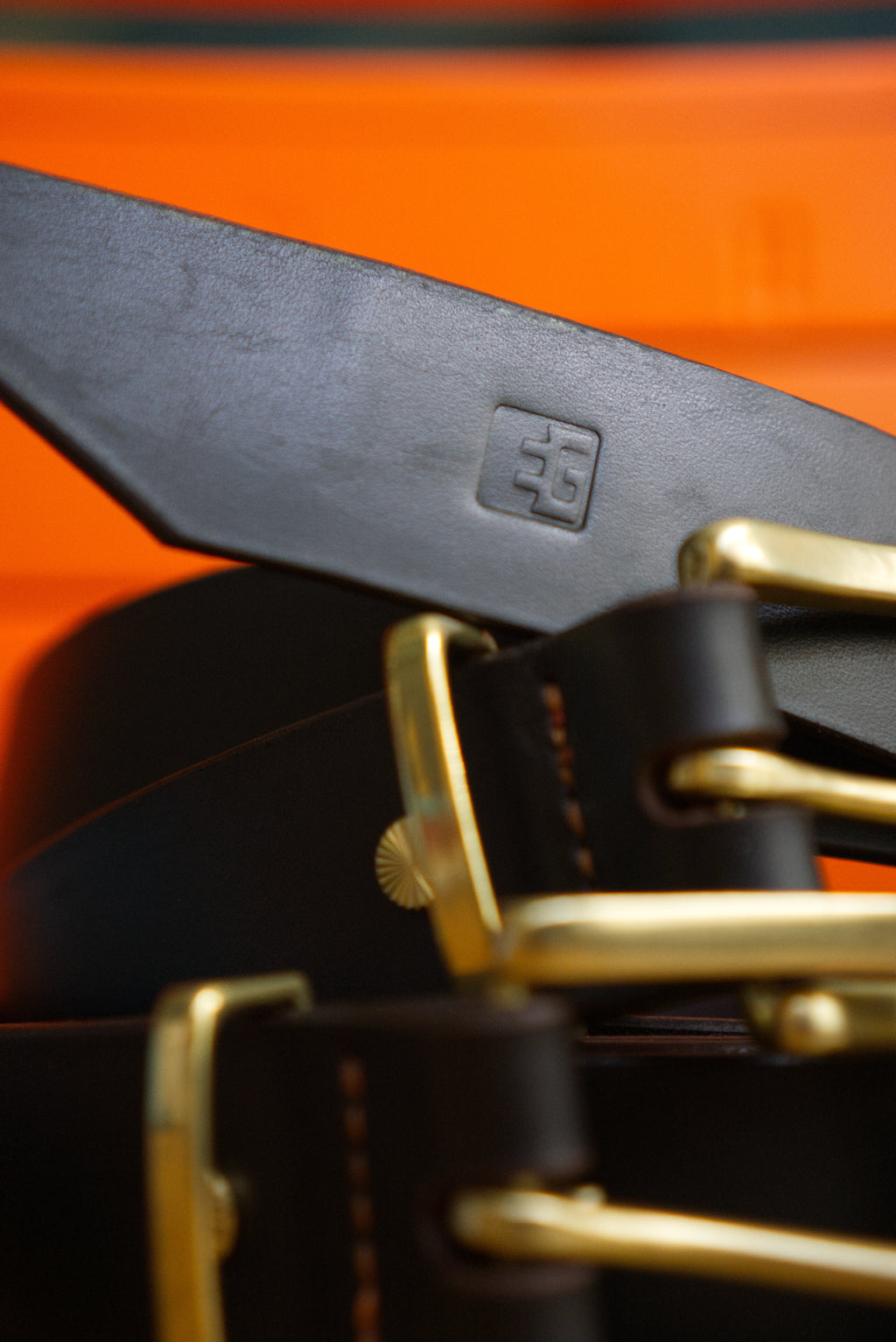 Close-up of a brown belt with brass hardware on an orange background