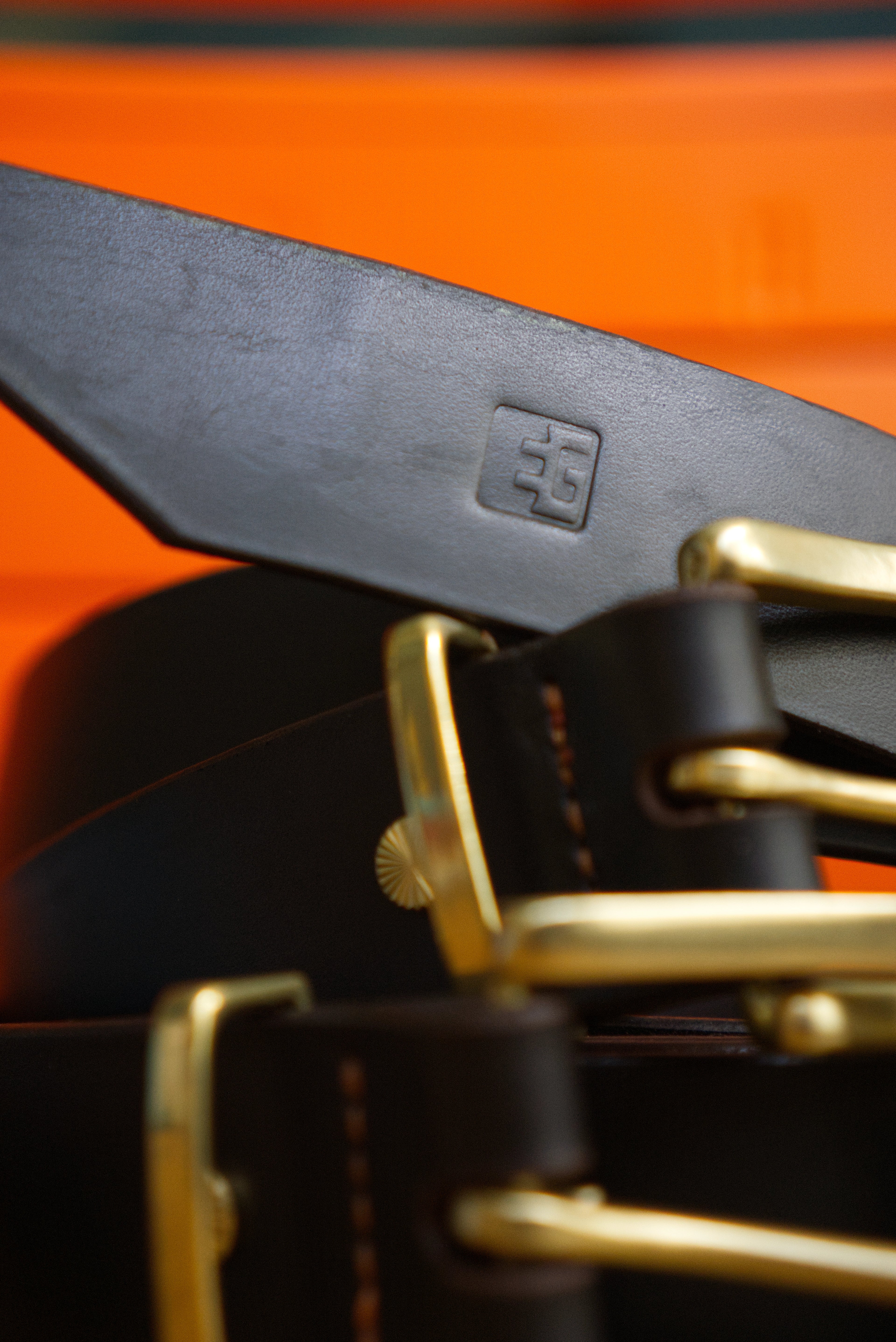 Close-up of a brown belt with brass hardware on an orange background