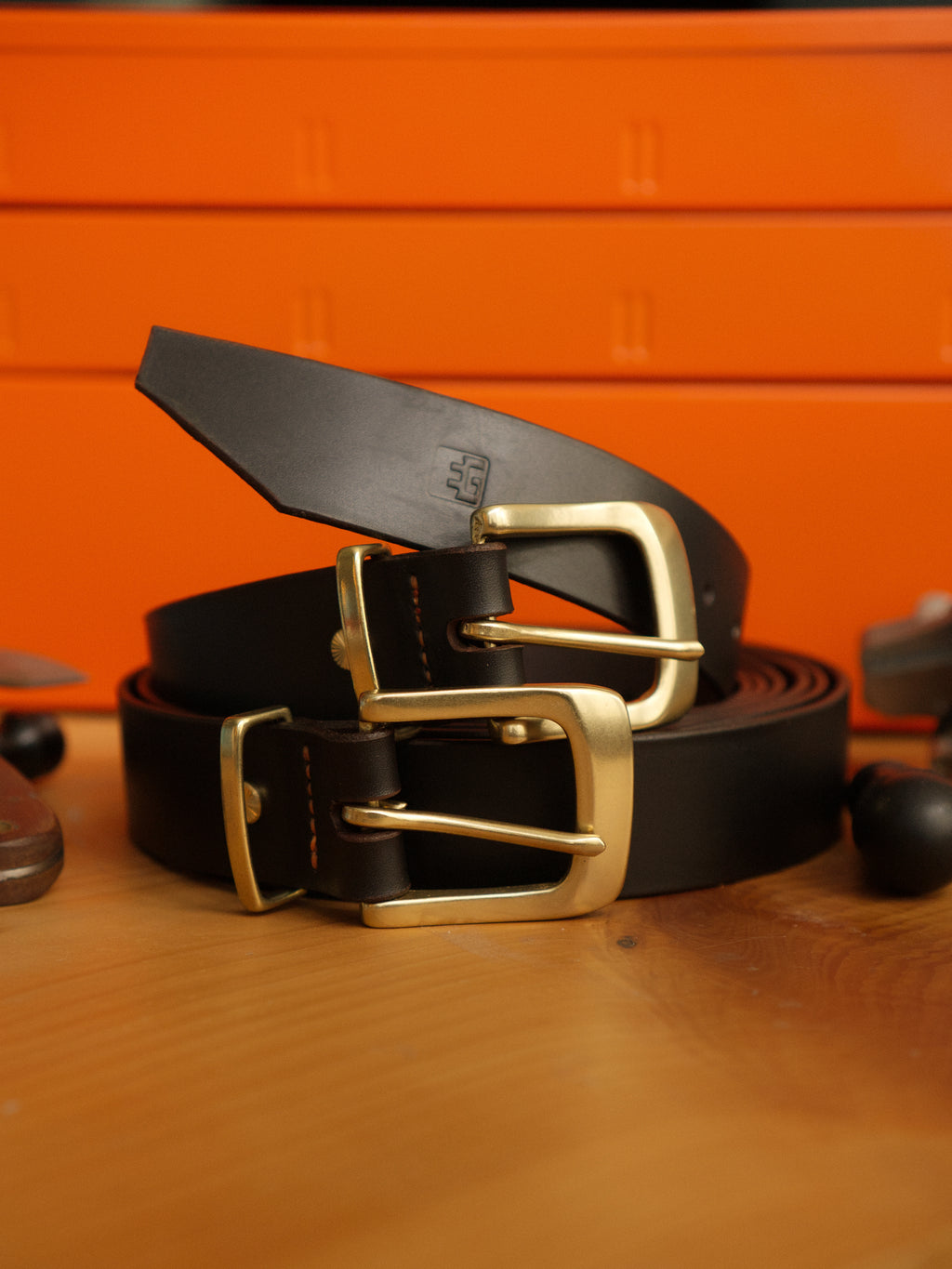 Brown leather belt with brass buckle on a wooden surface against an orange background